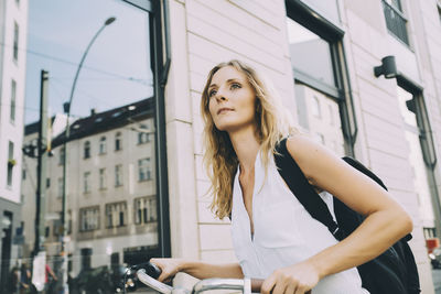 Female entrepreneur with bicycle standing against building in city