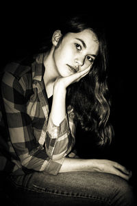 Portrait of woman sitting against black background