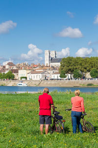 Rear view of senior couple with bicycles standing amidst plants against sky