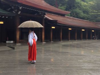 Rear view of woman with umbrella walking in building during rainy season