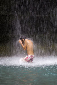 Shirtless boy bathing in waterfall