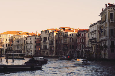 Boats in canal amidst buildings in city against clear sky