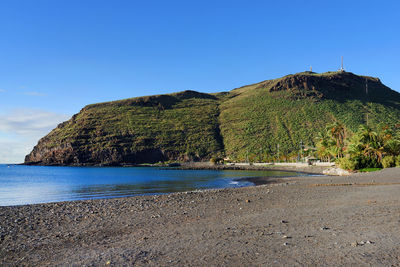 Scenic view of mountain by sea against blue sky