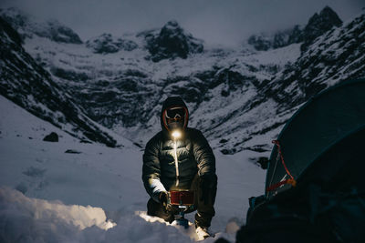 Man making tea close to the tent in switzerland mountains winter