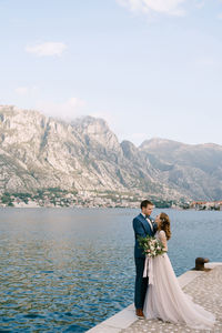 Rear view of couple walking on lake against mountains