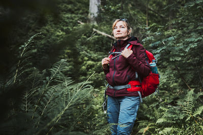 Woman with backpack hiking in forest, actively spending summer vacation close to nature