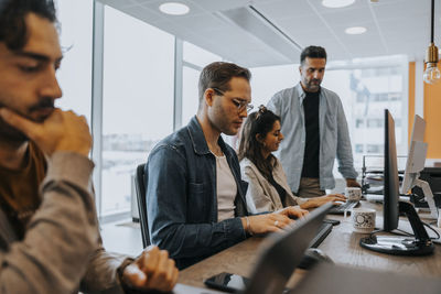 Businessman discussing strategy with businesswoman by colleagues working at office