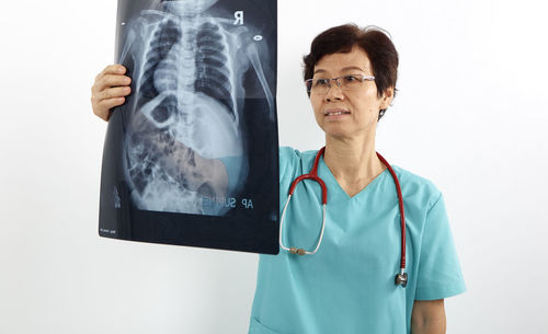 Female doctor looking medical x-ray while standing against white background