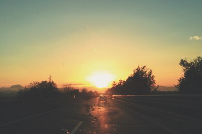Road by silhouette trees against sky during sunset