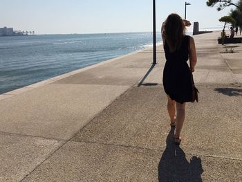 Rear view full length of woman walking by sea on walkway during sunny day