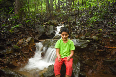 Full length of boy standing on rock in forest by waterfall