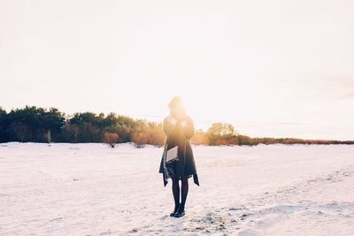 Full length of woman standing on snow covered field against clear sky