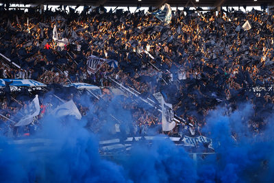 Argentine soccer fans welcome their team with flags, confetti and blue smoke inside a stadium 