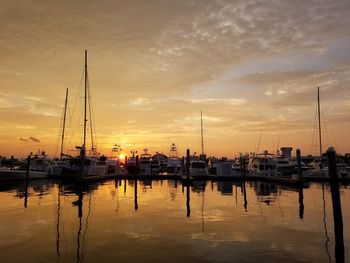 Sailboats moored at harbor against sky during sunset