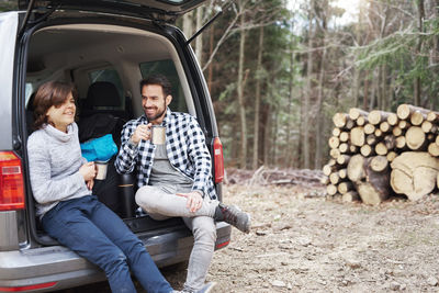 Father and son having coffee while sitting in car trunk during camping
