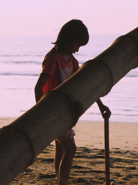 Boy holding wooden post by bamboo at beach