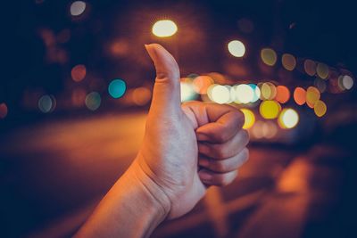 Close-up of human hand gesturing against illuminated street