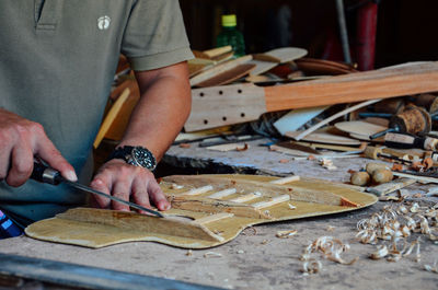 Midsection of man making guitar on table