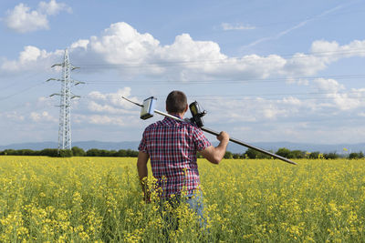 Rear view of engineer with equipment standing on oilseed rape field