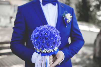 Midsection of man holding bouquet against blue sky
