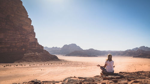 Woman meditating on landscape against clear sky