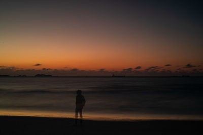 Silhouette man standing on beach against sky during sunset