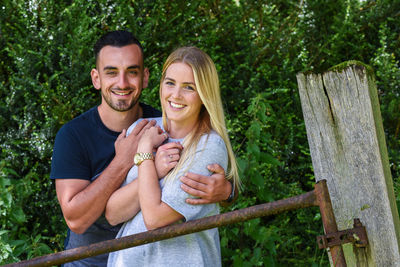 Portrait of smiling boyfriend embracing girlfriend against plants