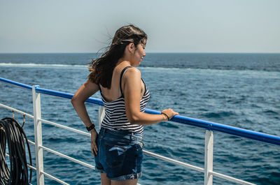 Young woman standing on railing against sea