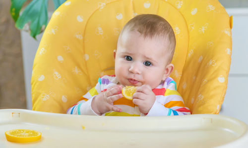 Cute baby girl eating orange fruit at home