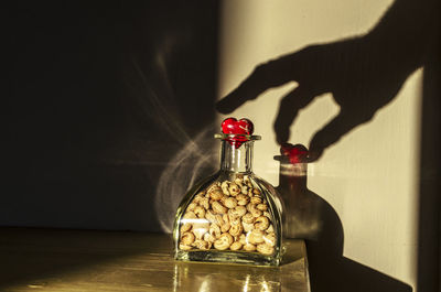 Close-up of hand holding glass bottle on table against wall