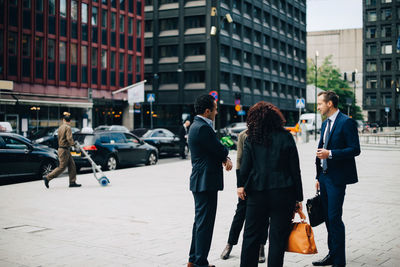 Male and female business colleagues standing on sidewalk against buildings in city