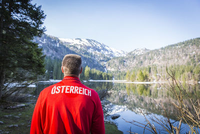 Rear view of man looking at lake against sky