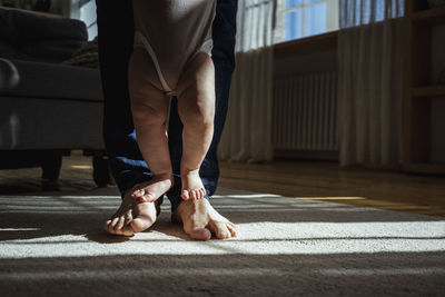 Baby girl standing on father's feet at home