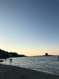 Silhouette people on beach against clear sky during sunset