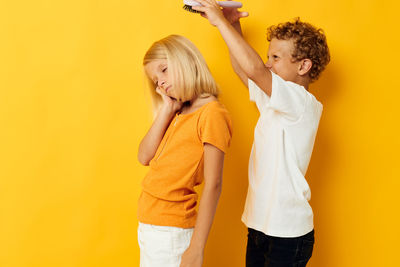 Boy combing sisters hair against yellow background