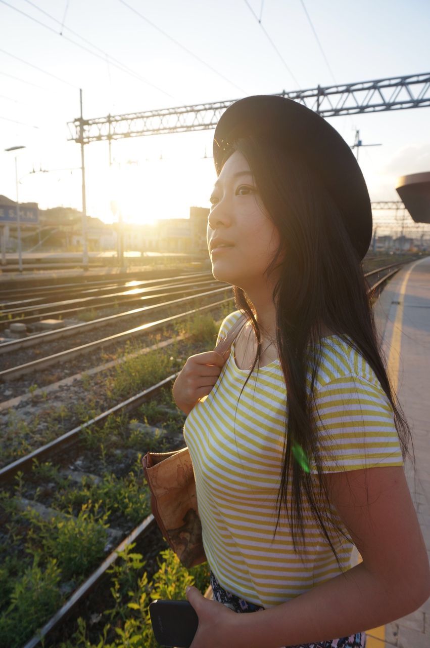 lifestyles, railroad track, person, casual clothing, transportation, leisure activity, rail transportation, sunlight, young adult, young women, looking away, holding, day, full length, portrait, outdoors, rear view, side view