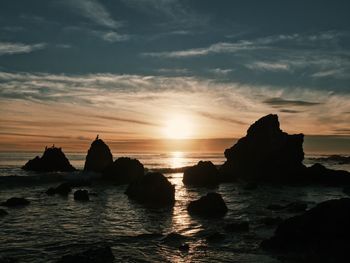 Silhouette rock formation in sea against sky during sunset