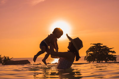 Silhouette people by sea against sky during sunset