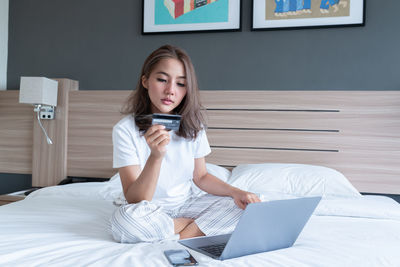 Young woman using phone while sitting on bed