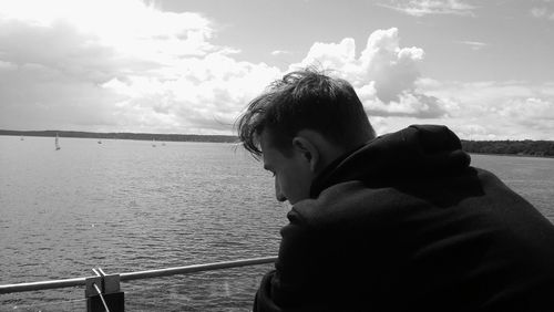 Thoughtful man sitting by lake against sky