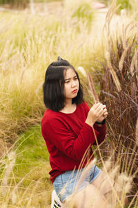 Young woman looking at plant while kneeling on field