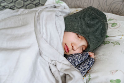 Close-up of cute boy in warm hat sleeping on bed