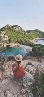 Rear view of woman sitting on rock by mountain against sky