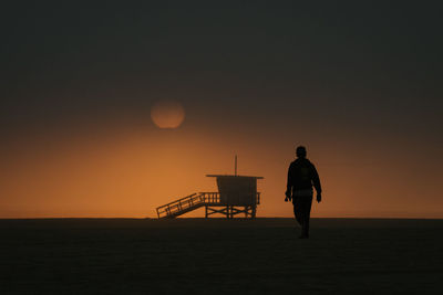 Skateboarder walking towards moody sunset in venice beach, ca usa