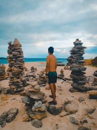 Rear view of shirtless man standing on rock at beach against sky