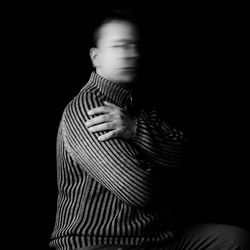 Man shaking head while sitting with arms crossed against black background