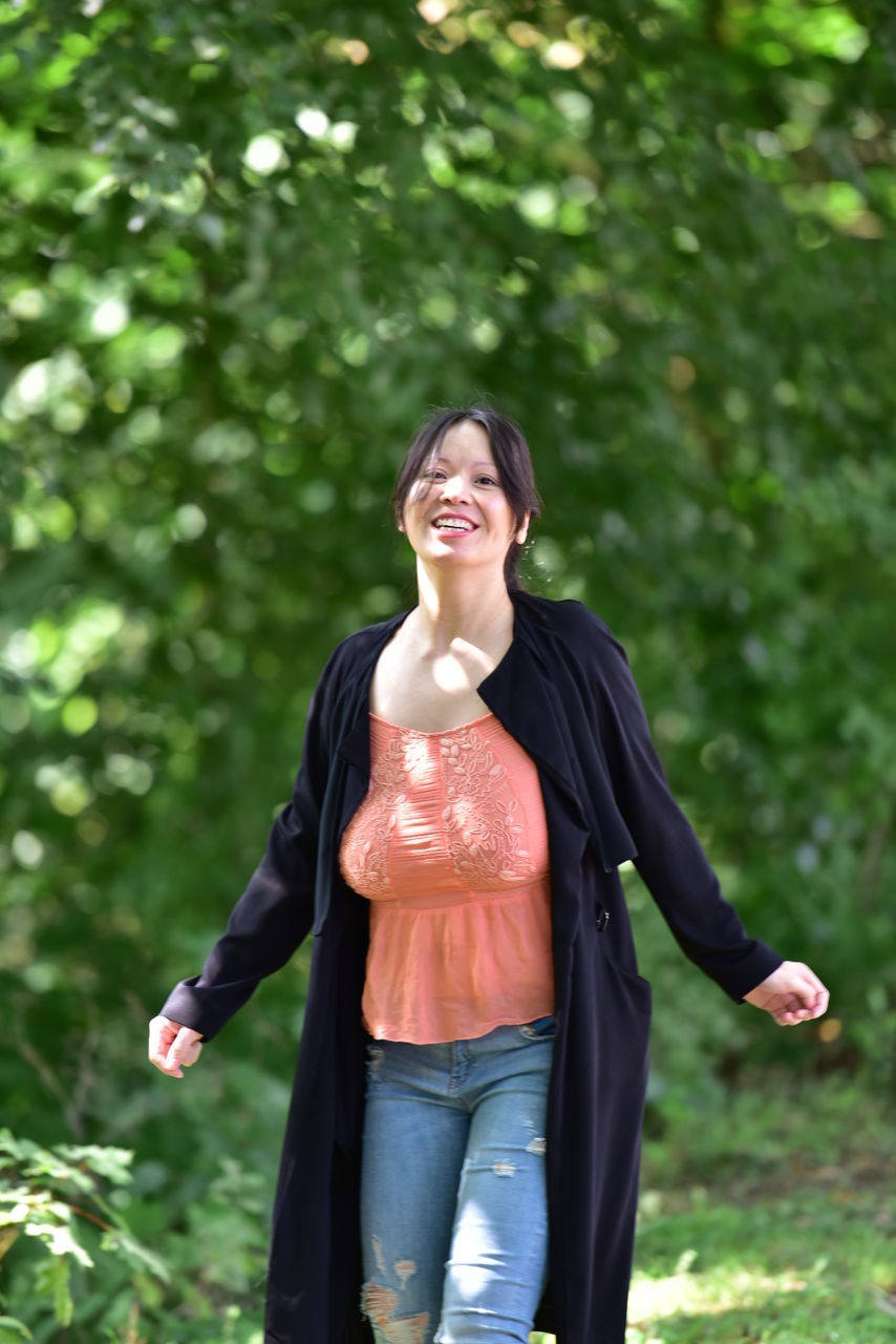 smiling, lifestyles, one person, real people, outdoors, casual clothing, leisure activity, young adult, young women, happiness, day, front view, standing, walking, tree, nature, cheerful, beautiful woman