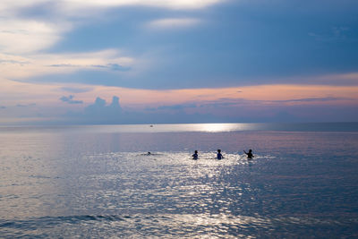 Silhouette people on sea against sky during sunset