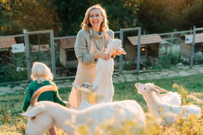 Happy smiling woman and little girl feed goats on the farm. rural life, recreation with animals.