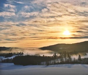 Scenic view of snowcapped landscape against cloudy sky at sunset